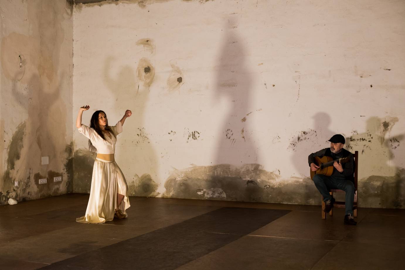 In white, Rocio Molina extends her arms in a room of her farmhouse as a guitarist plays